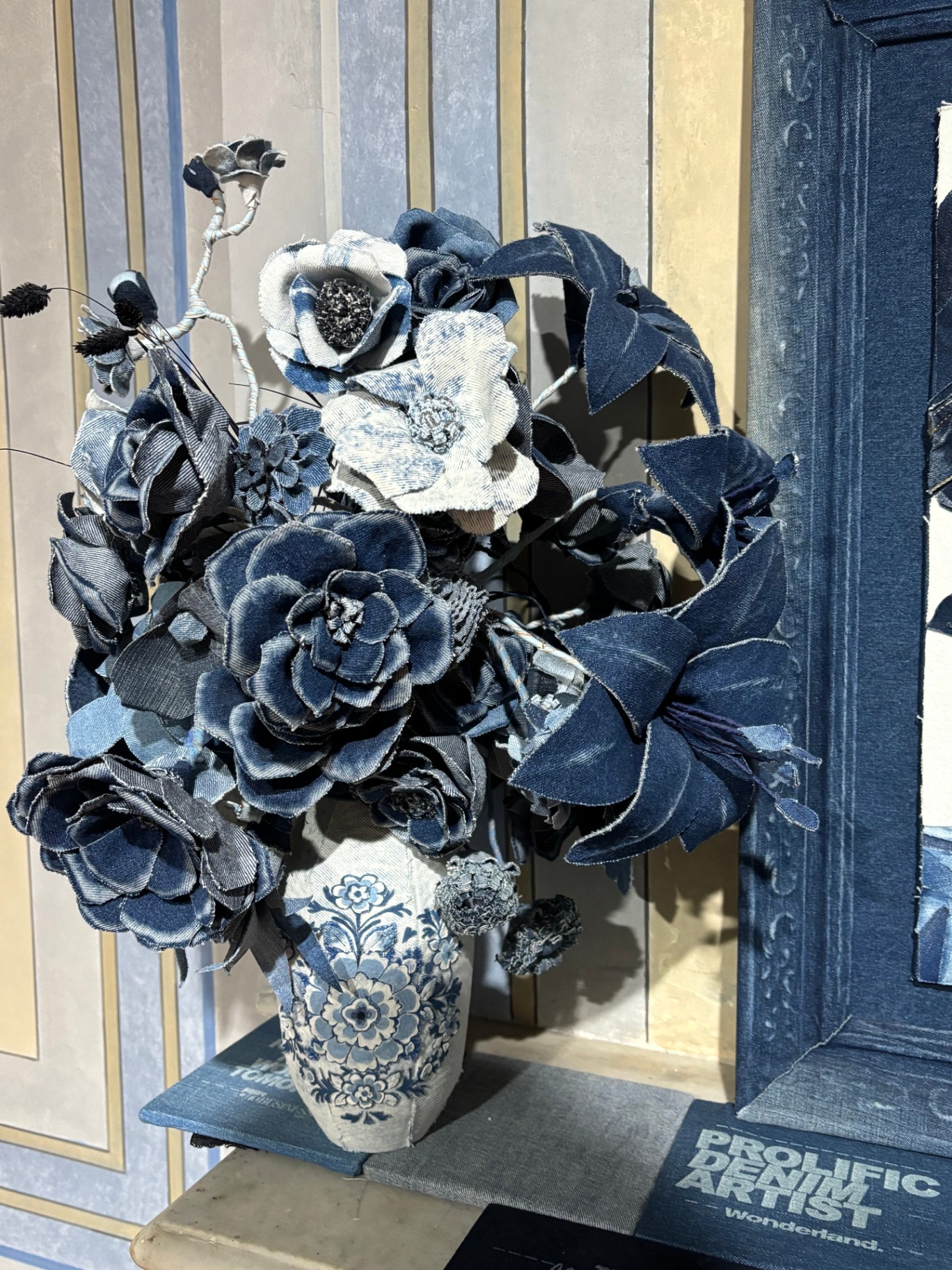 A bouquet of artificial denim flowers in a decorative vase, placed on a surface next to a Prolific Dream Artist book.