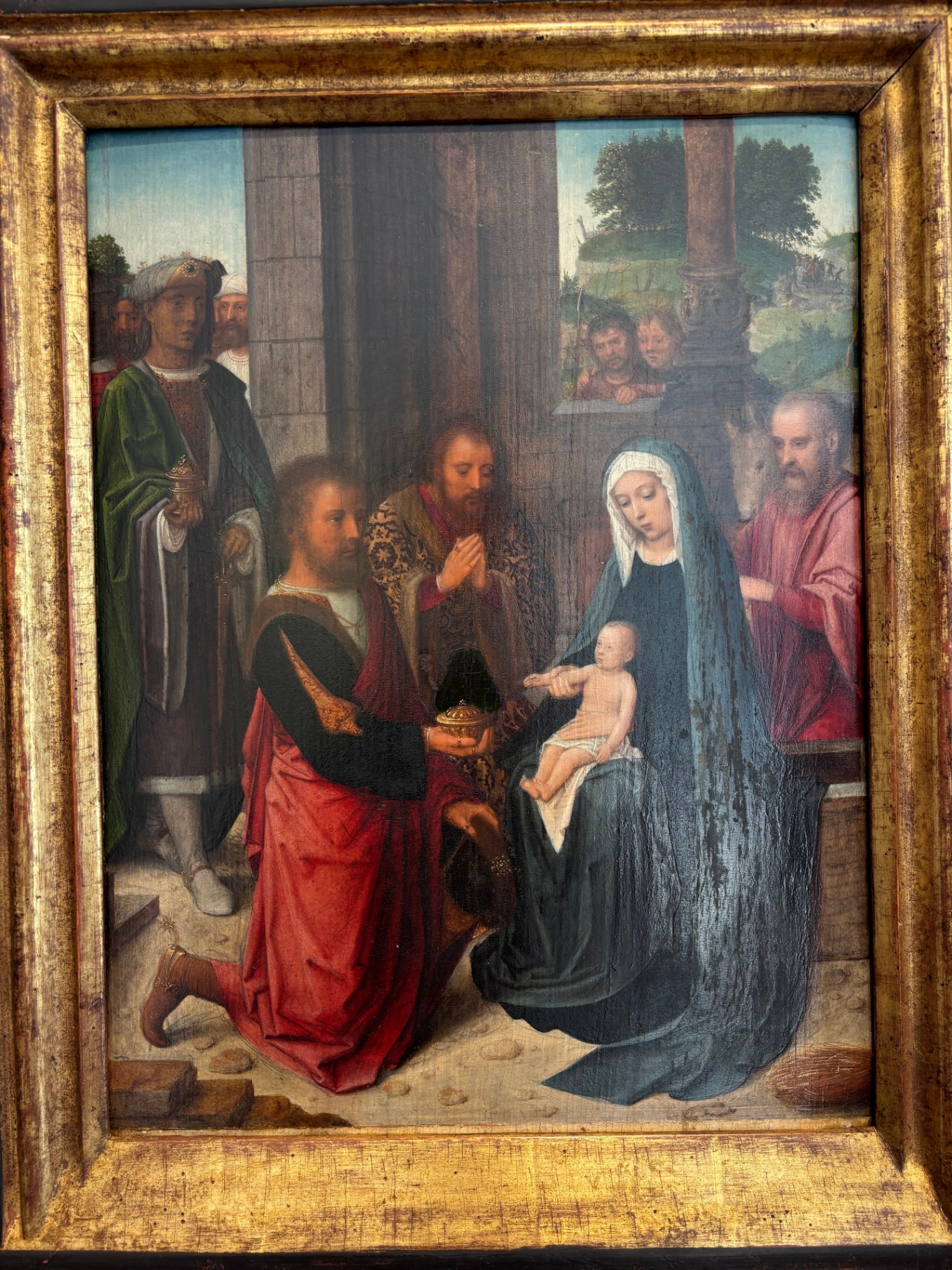 Painting of the Madonna and Child with several saints and onlookers, set in an interior with a landscape visible through an open window.