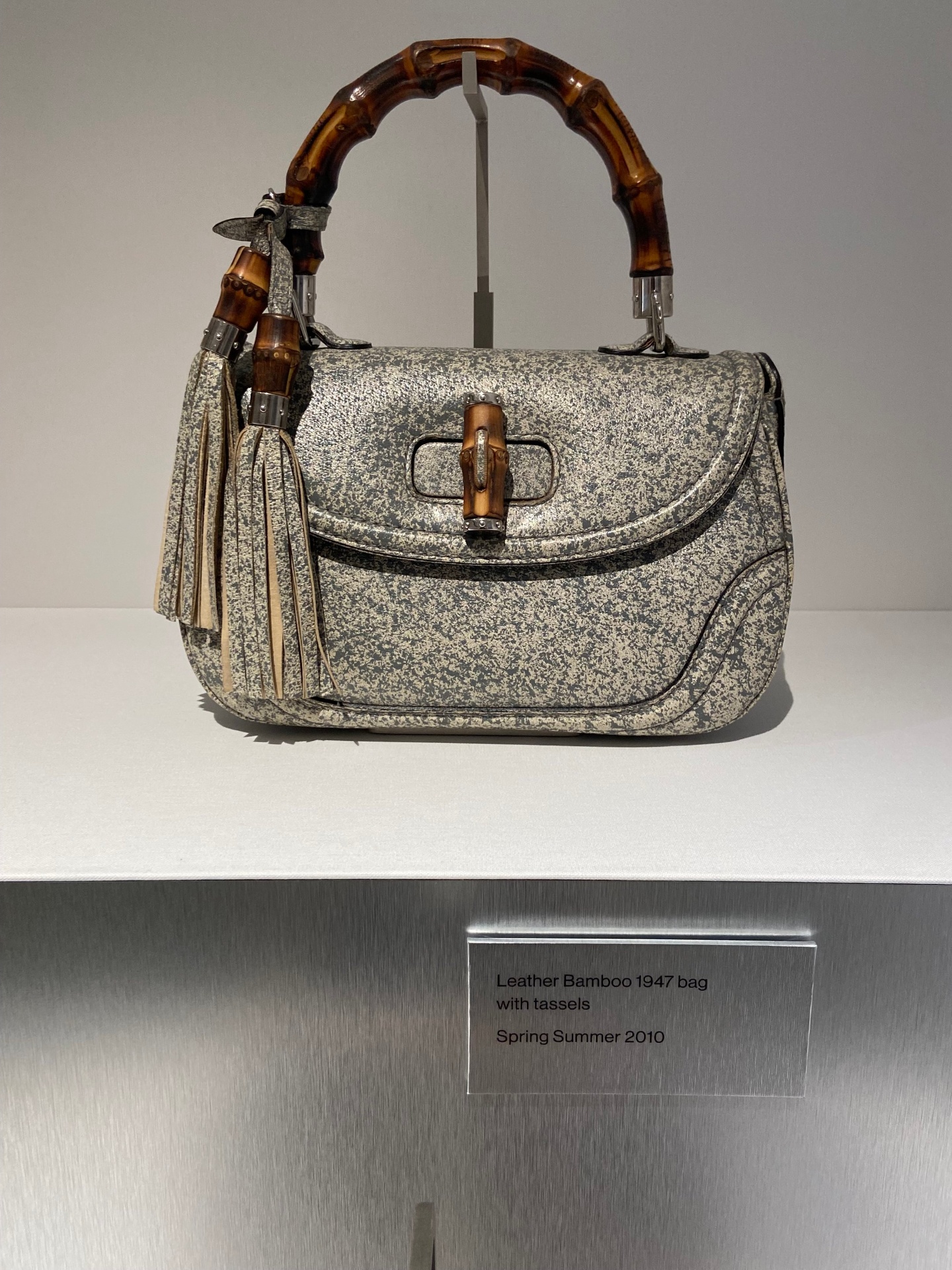Leather bamboo handbag from 1947 with tassels, displayed on a stand at a museum exhibit, labeled as Spring Summer 2010.