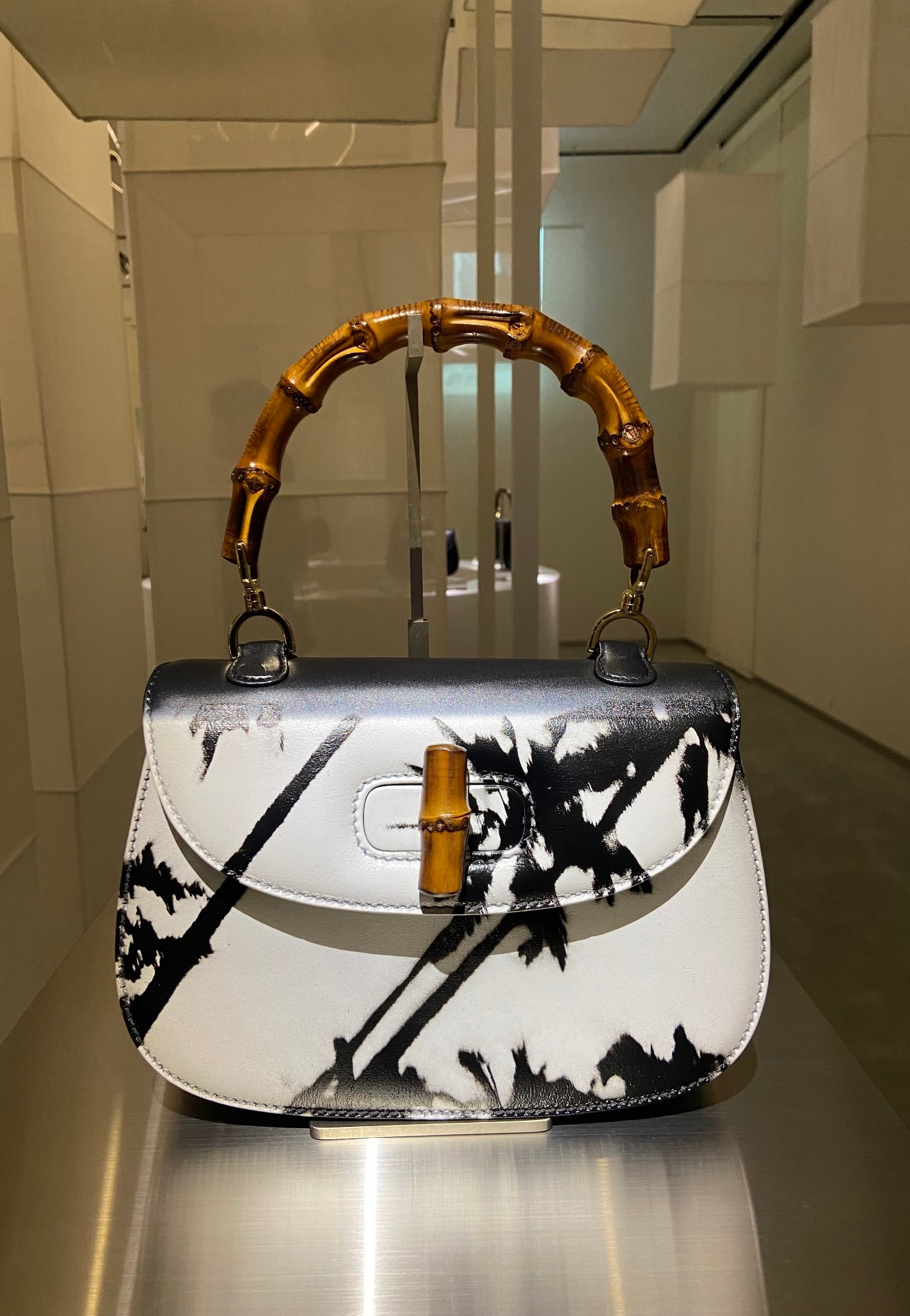 A designer handbag with a black and white abstract pattern, bamboo handle, and bamboo clasp on display in a well-lit, modern interior.