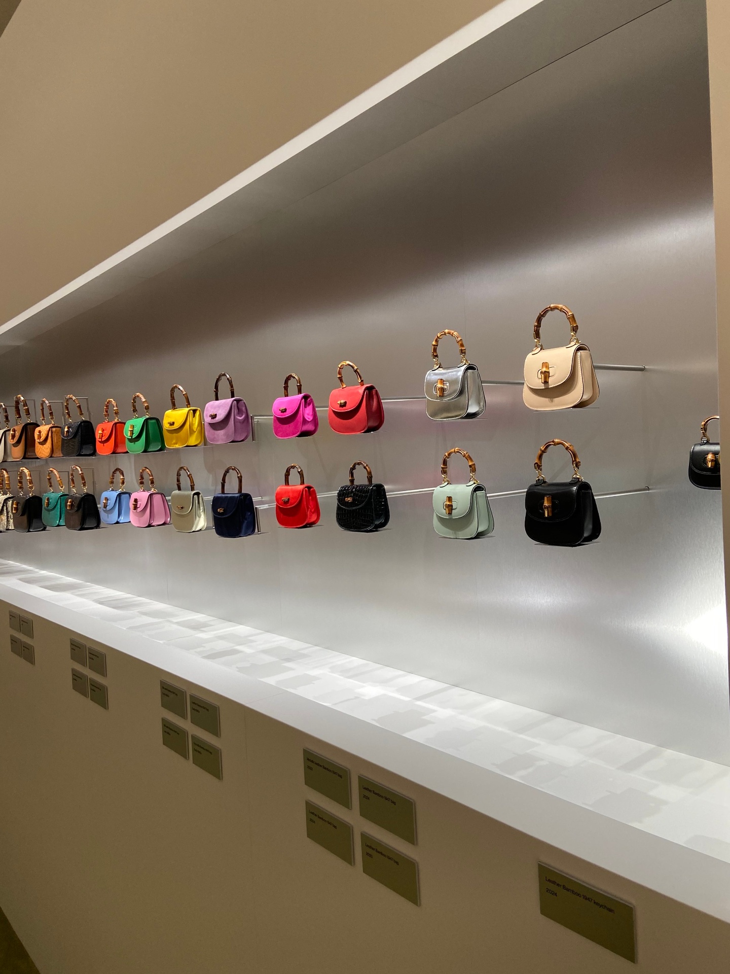 Display of colorful handbags on wall shelves at a store with labels underneath.