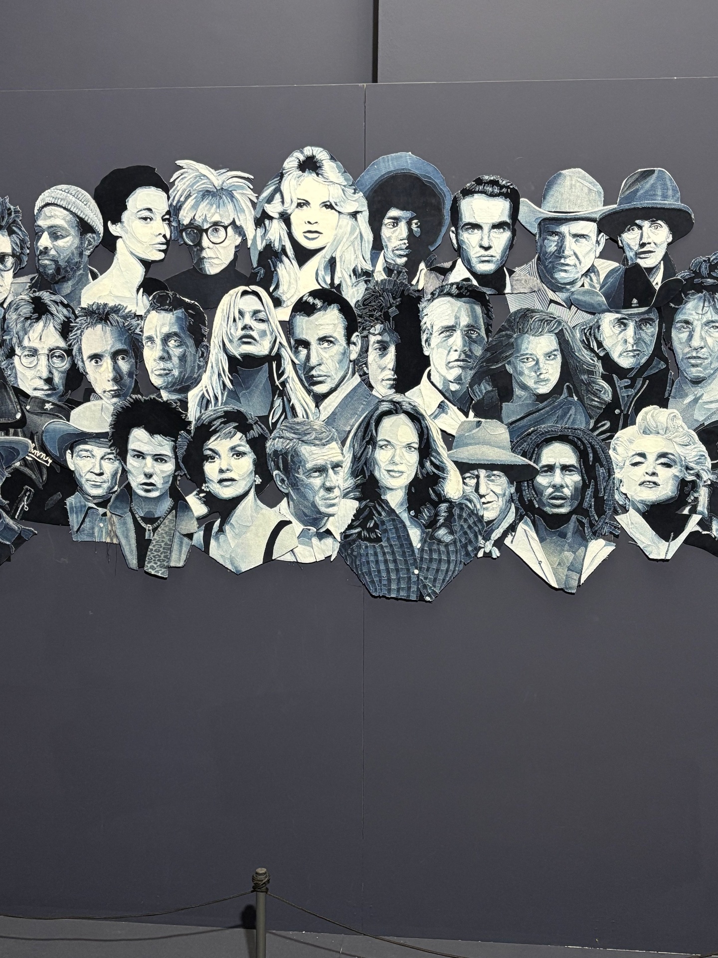A mural of black and white portraits of various famous people in a collage style on a dark wall.