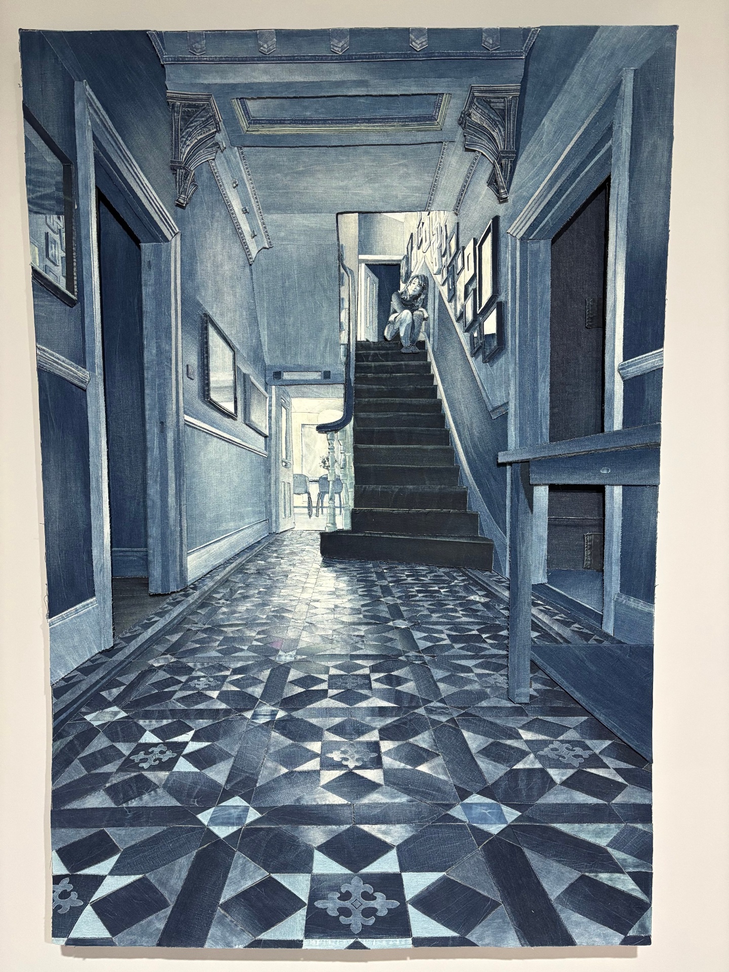 A black and white painting of an interior hallway with patterned tile floor, staircase at the front, and walls decorated with framed photos; a person is sitting on the top of the stairs.